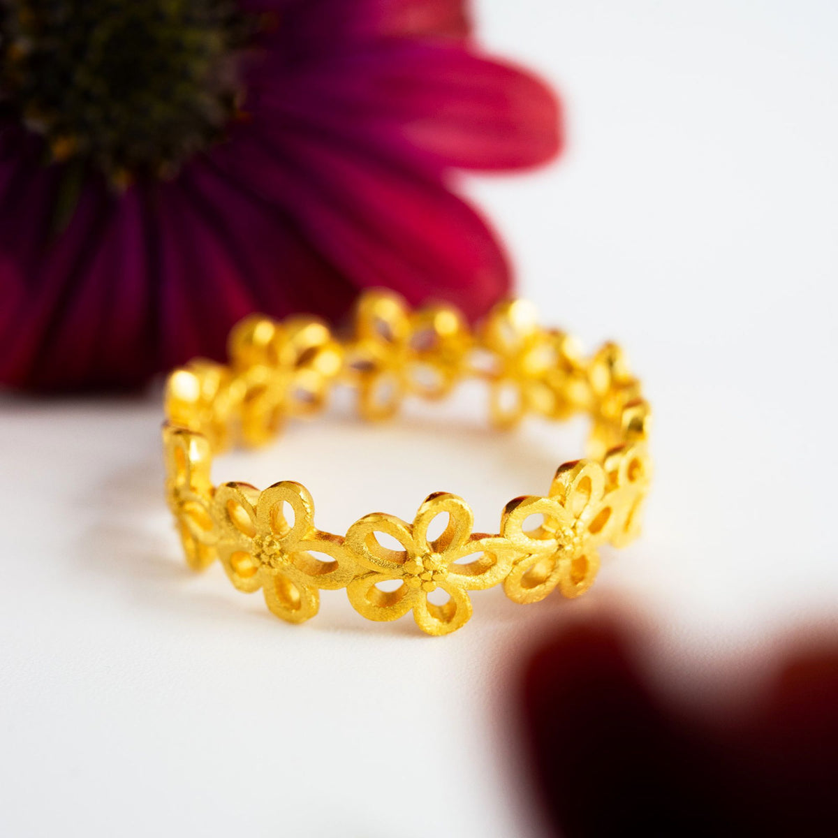 Vergoldeter Ring mit floralem Blütendesign aus der BERND WOLF Schmuckmanufaktur vor dekorativem Blütenhintergrund.