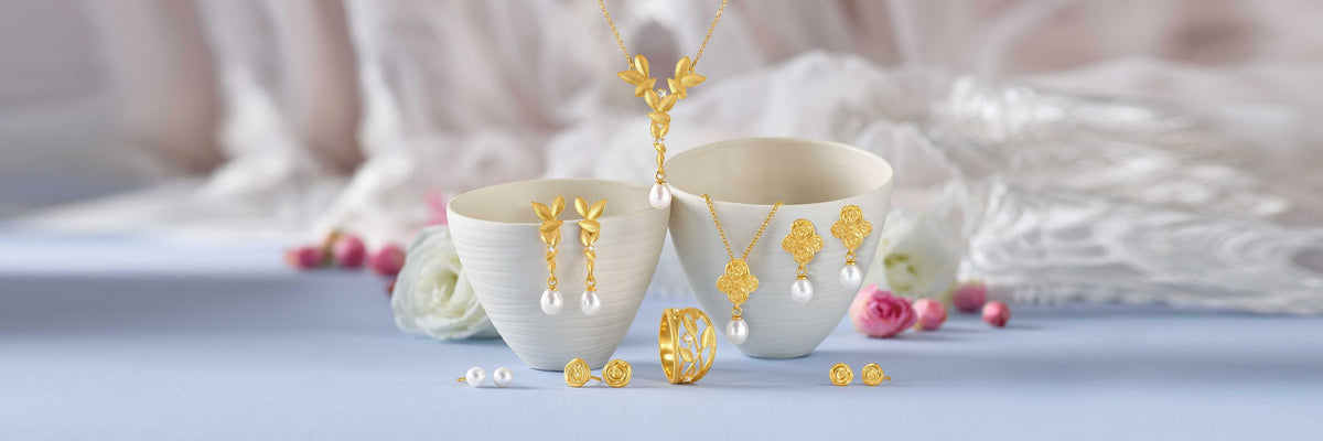 Goldener Brautschmuck mit Perlen, Halskette, Ohrhängern, Ohrsteckern und Ring vor heller Hochzeitsdekoration