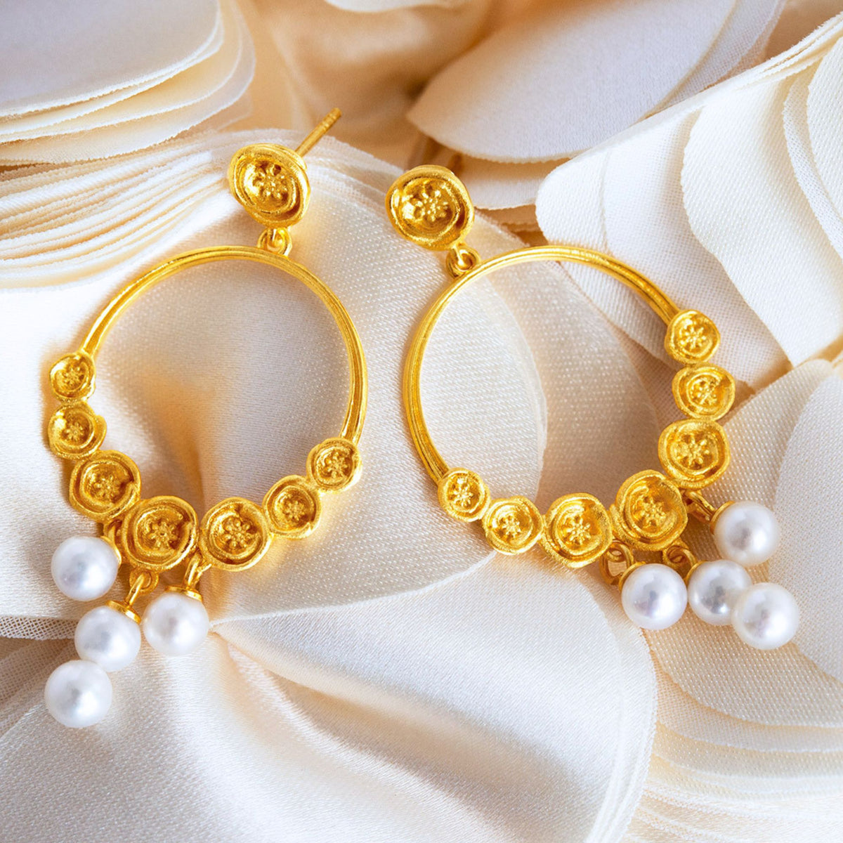 Vergoldete Creolen mit weißen Perlen als eleganter Brautschmuck auf cremefarbenem Stoff arrangiert.