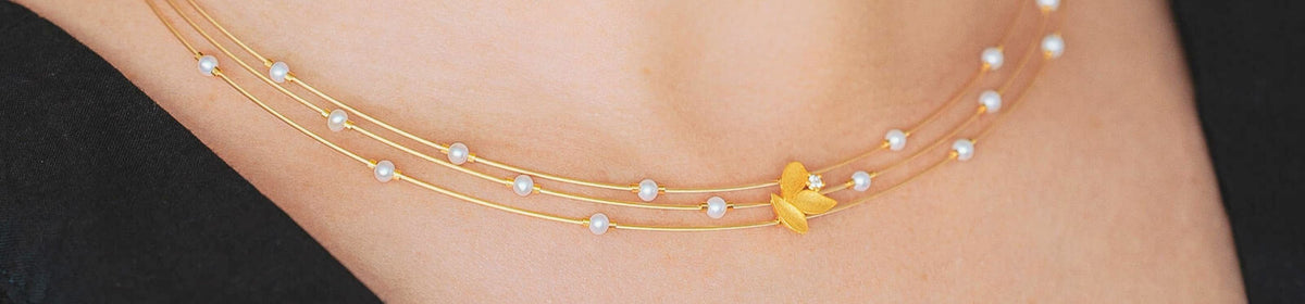 Goldenes BERND WOLF Collier mit weißen Perlen und floralem Schmuckelement