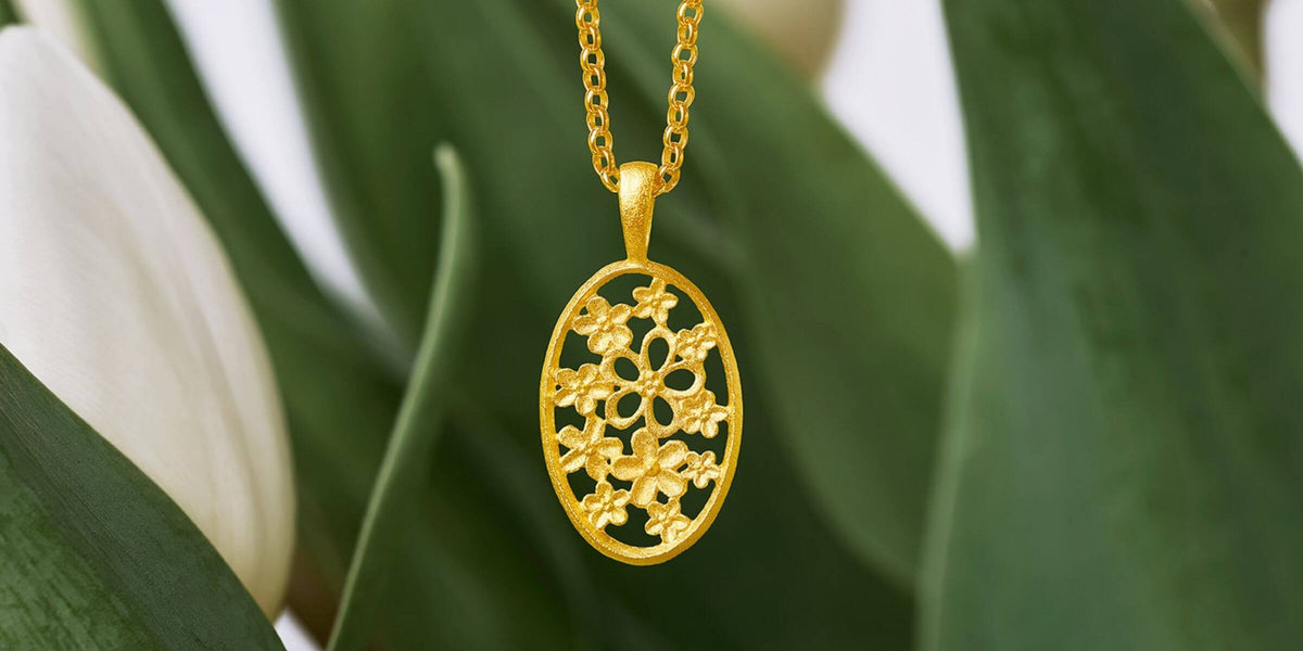 Nachhaltig gefertigter Schmuck von BERND WOLF mit floralem Anhänger vor natürlichem Blätterhintergrund.